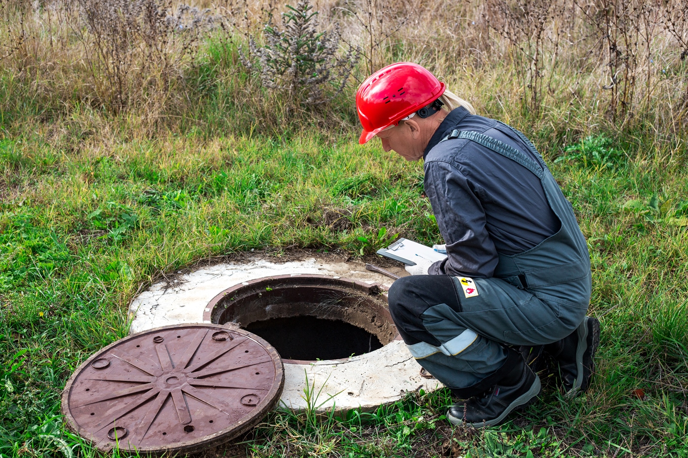 hydraulik-mezczyzna-w-kombinezonie-i-kasku-przy-studni-zapisuje-wykonane-pomiary-i-wskazania-wodomierza